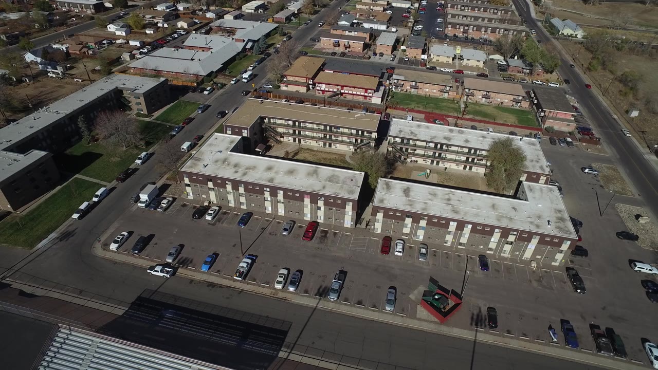 Overhead view of brick buildings, asphalt parking, and nearby houses.