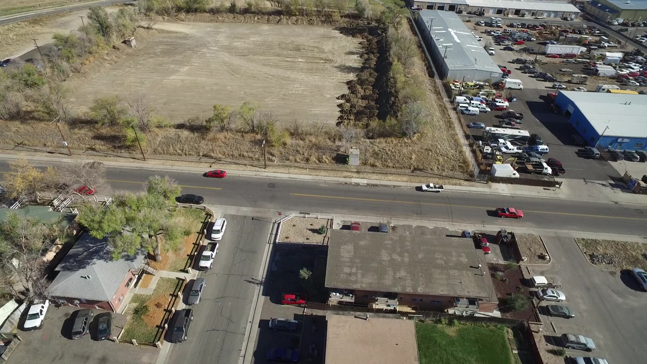 Overhead Westminster, Colorado frame with a red car and white car on the road, a large empty field beyond it, low commercial buildings, and no visible people.