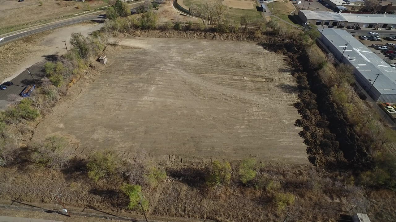 High aerial view of a dry brown field beside roads and low buildings.