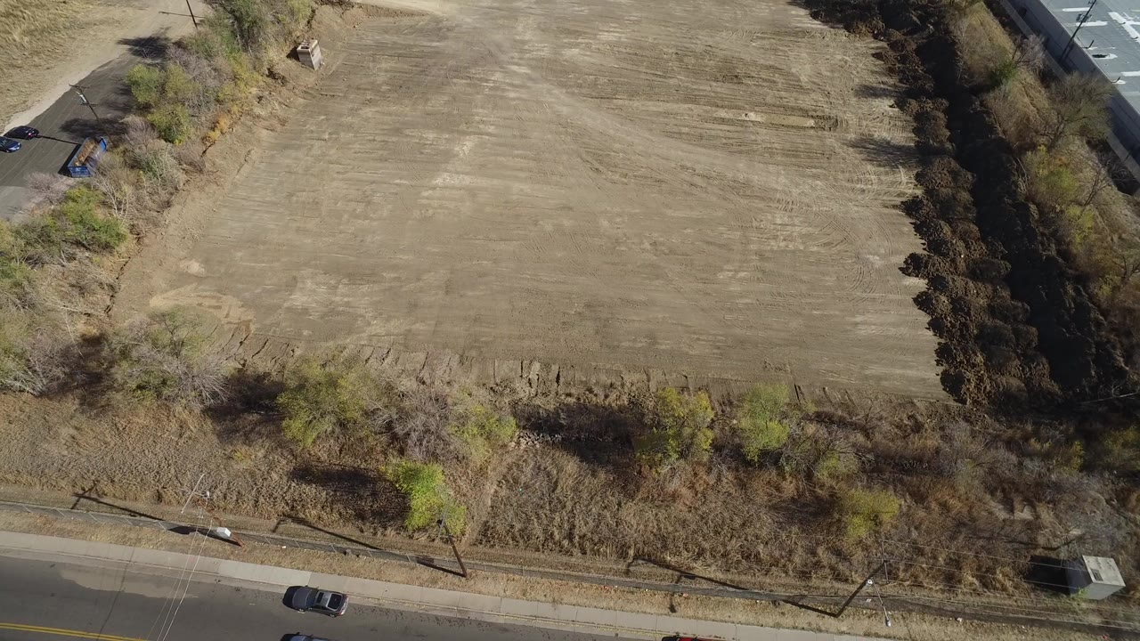 Aerial view of a bare field bordered by trees and a road.