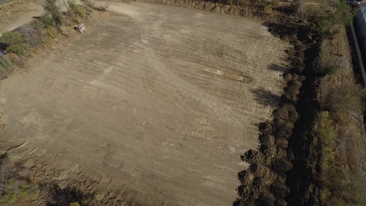 Overhead view of a tan dirt plot bordered by trees.