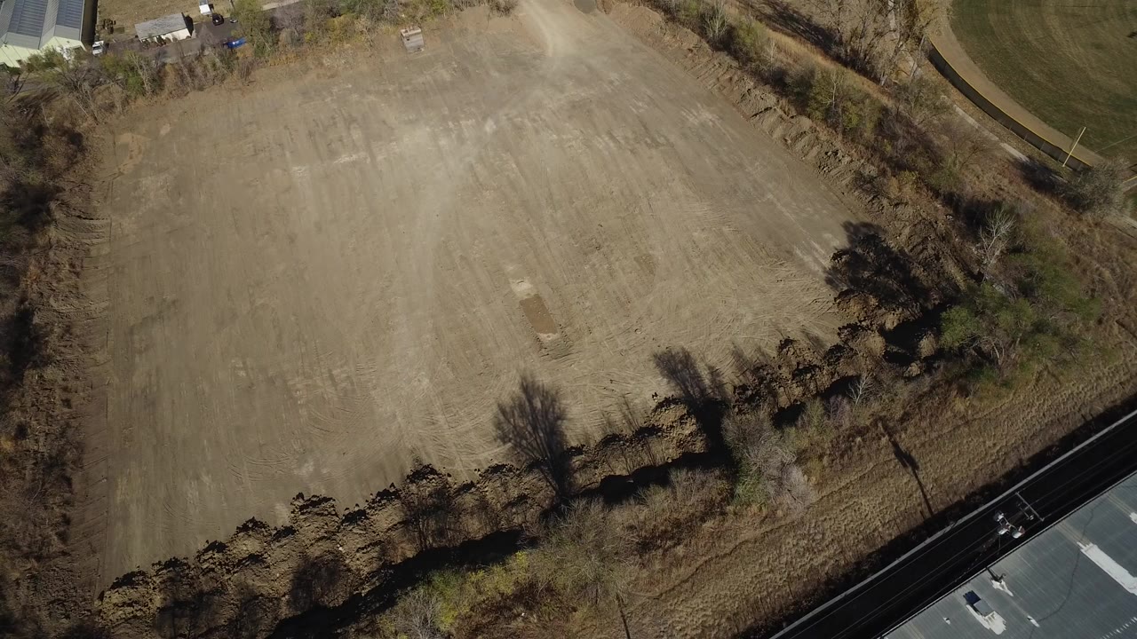 Overhead view of a tan dirt field bordered by trees and a road.