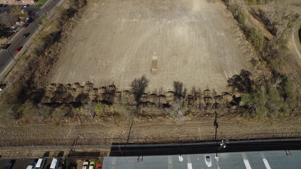 High overhead view of dry open land in Westminster, Colorado, with a road along the lower edge, trees and shrubs across the middle, and no visible people.
