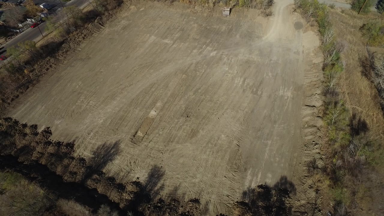 Aerial view of the Westminster field with broad tilled rows, a pale dirt access track near the upper right, brushy vegetation, and no visible people.