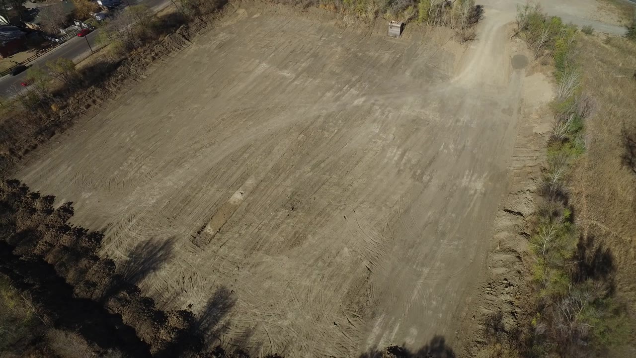 Overhead angled view of a dry plowed field with trees and a road near the top edge.