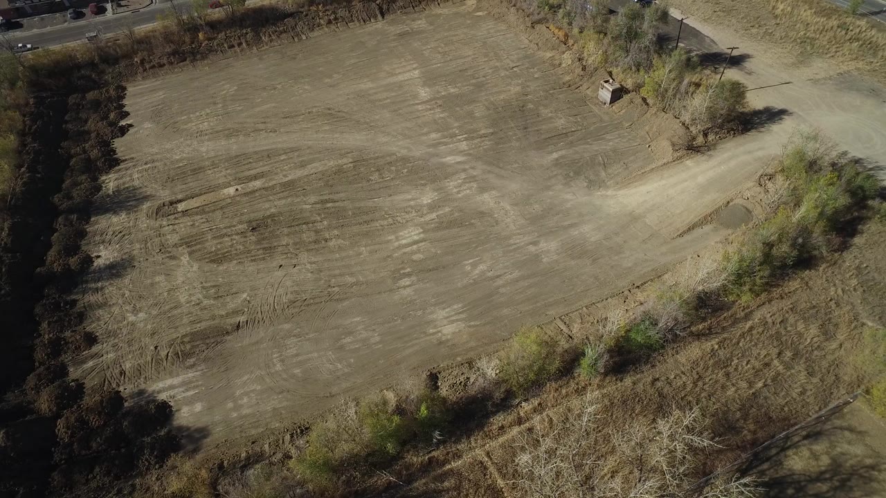 High aerial view of a dry field bordered by trees and brush.