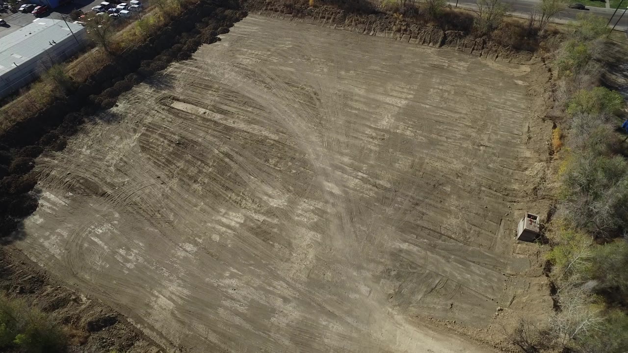 High aerial view of a cleared dirt lot bordered by trees and roads.