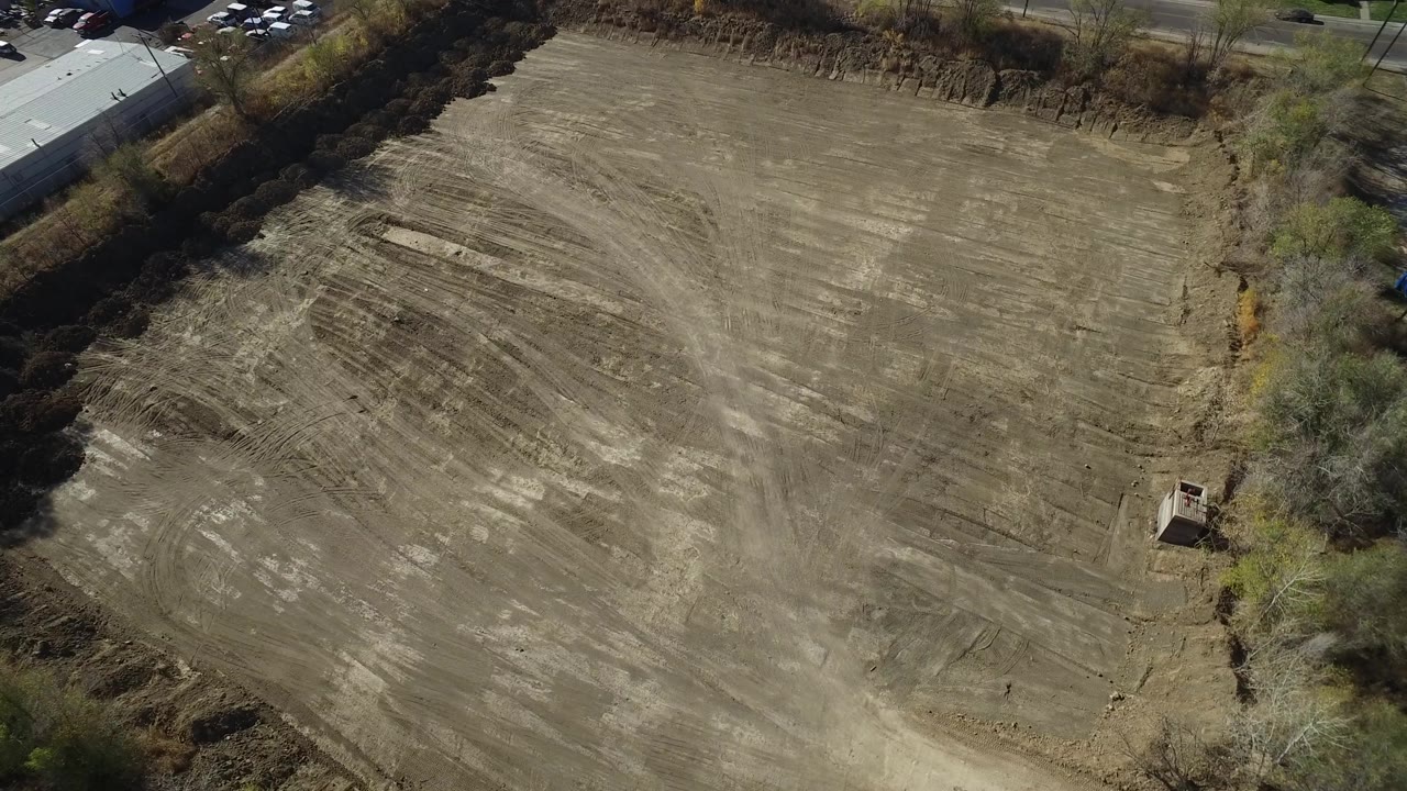 Aerial view in Westminster, Colorado, showing the scraped lot from a slightly shifted angle, with pale soil streaks, a road and building edge near the top, and no visible people.