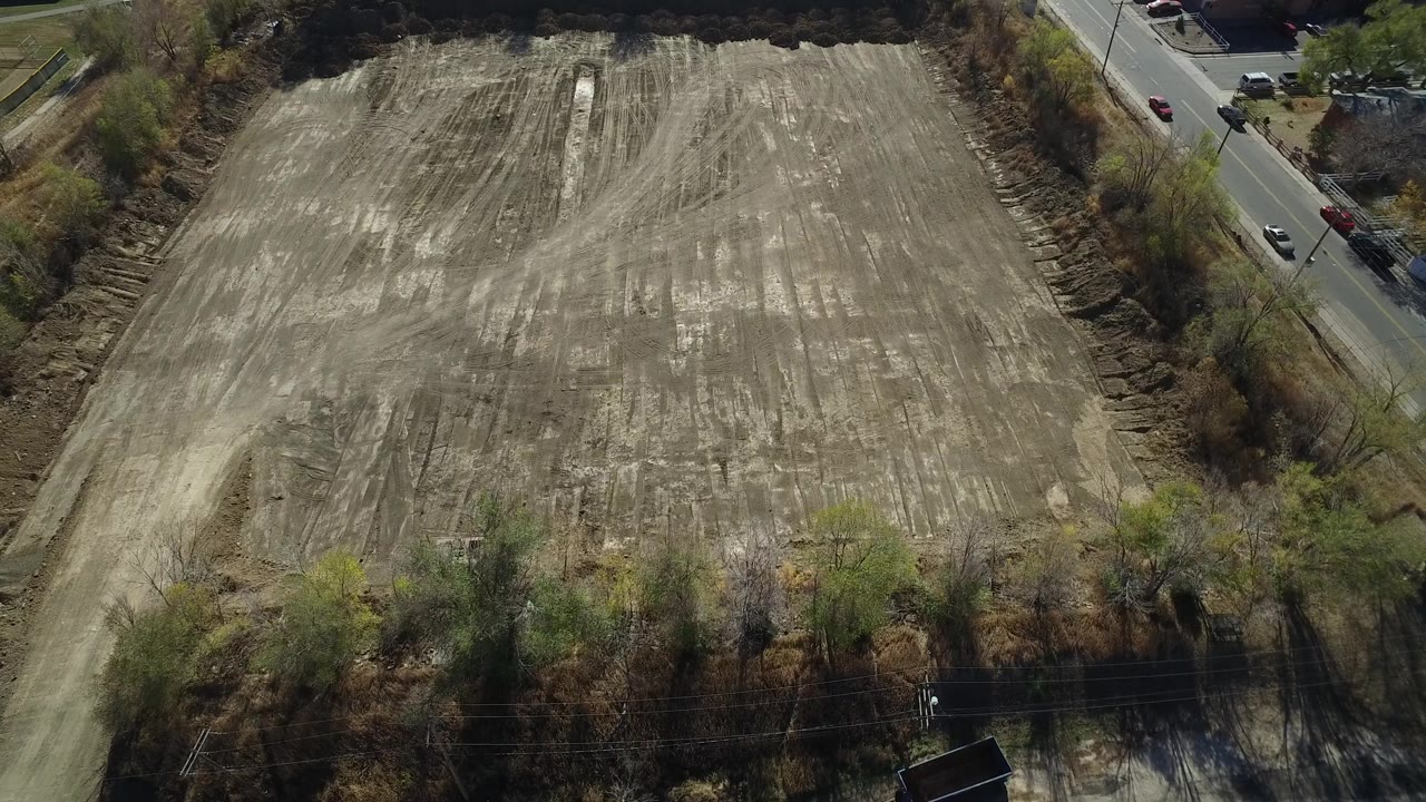 Elevated view of the Westminster dirt parcel with scraped tan ground, brush at the borders, a road carrying a few cars, and no visible people.