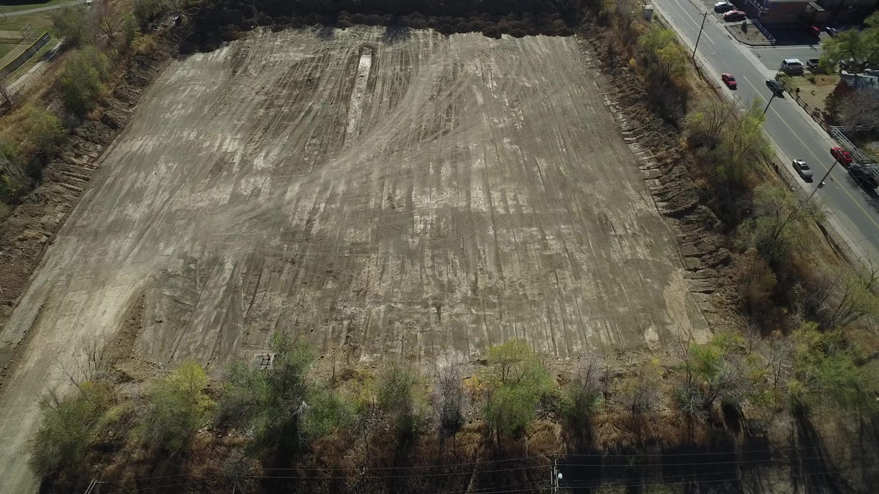 Aerial frame of an empty dirt field bordered by trees and roadside traffic.