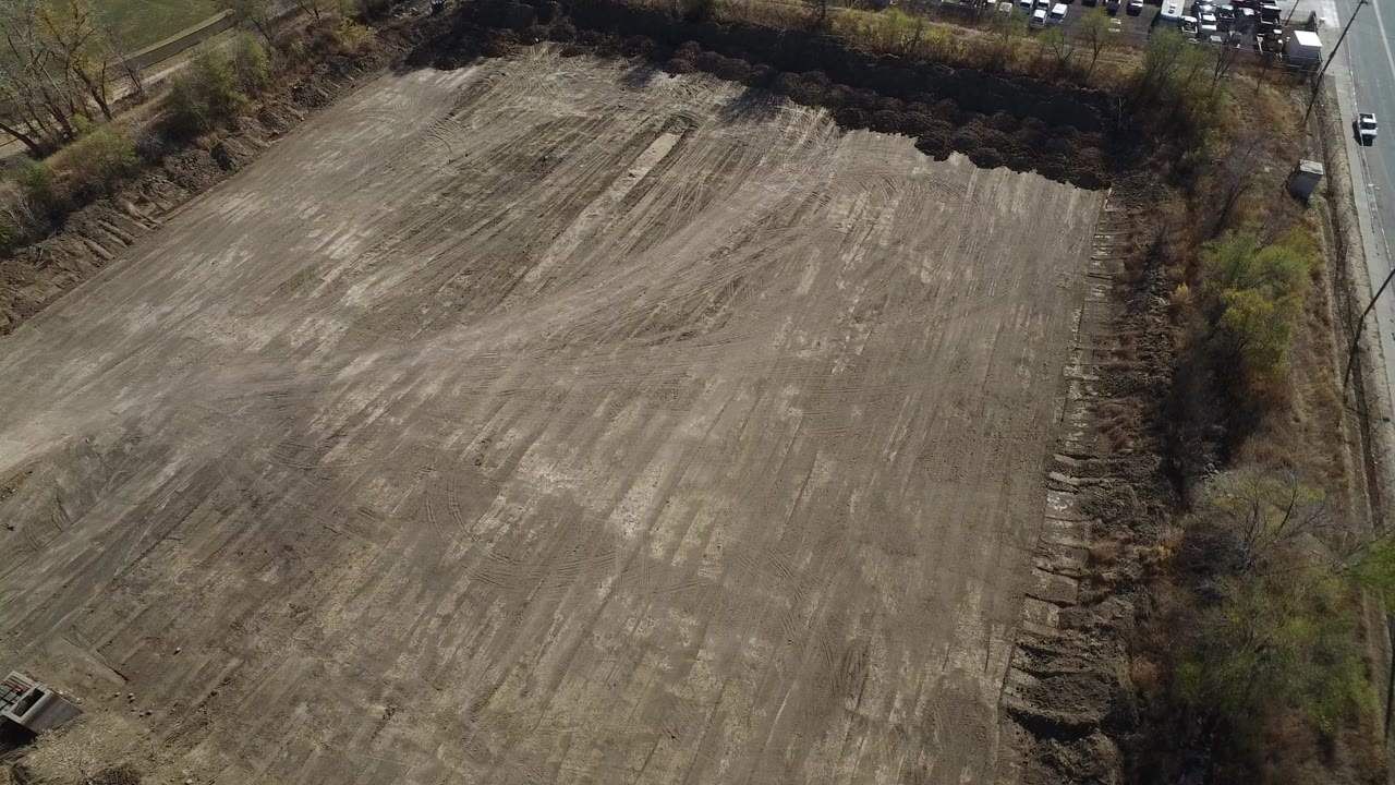 Aerial view of a large cleared dirt lot bordered by trees and a road.