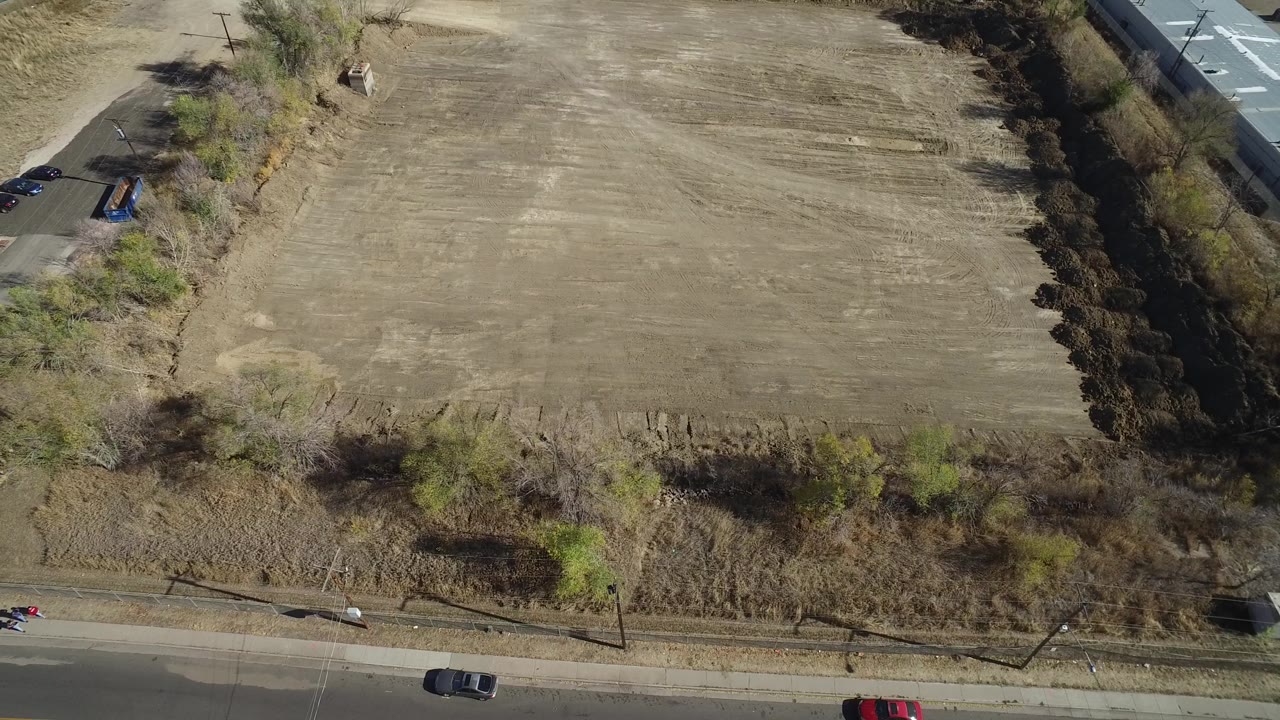 Aerial view of a roadside field with cars and a small figure near the road.
