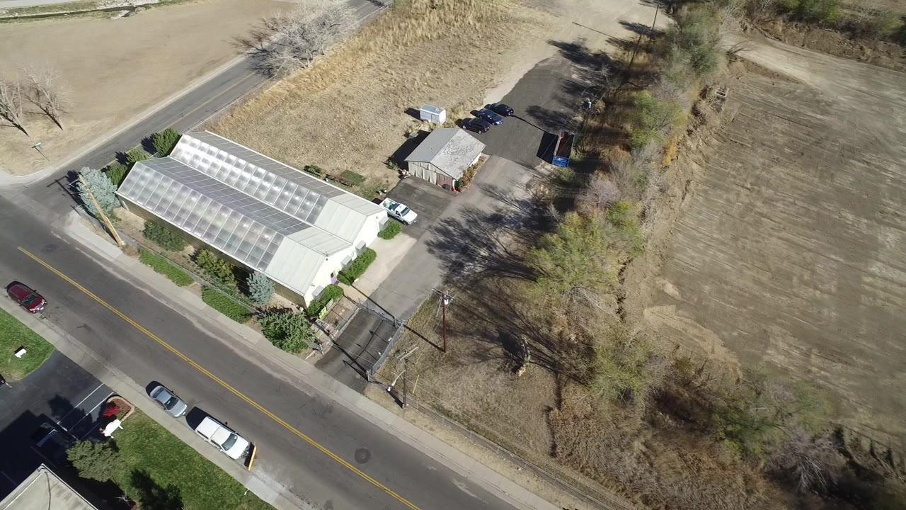Aerial view of a road beside a greenhouse-like building and dry field.