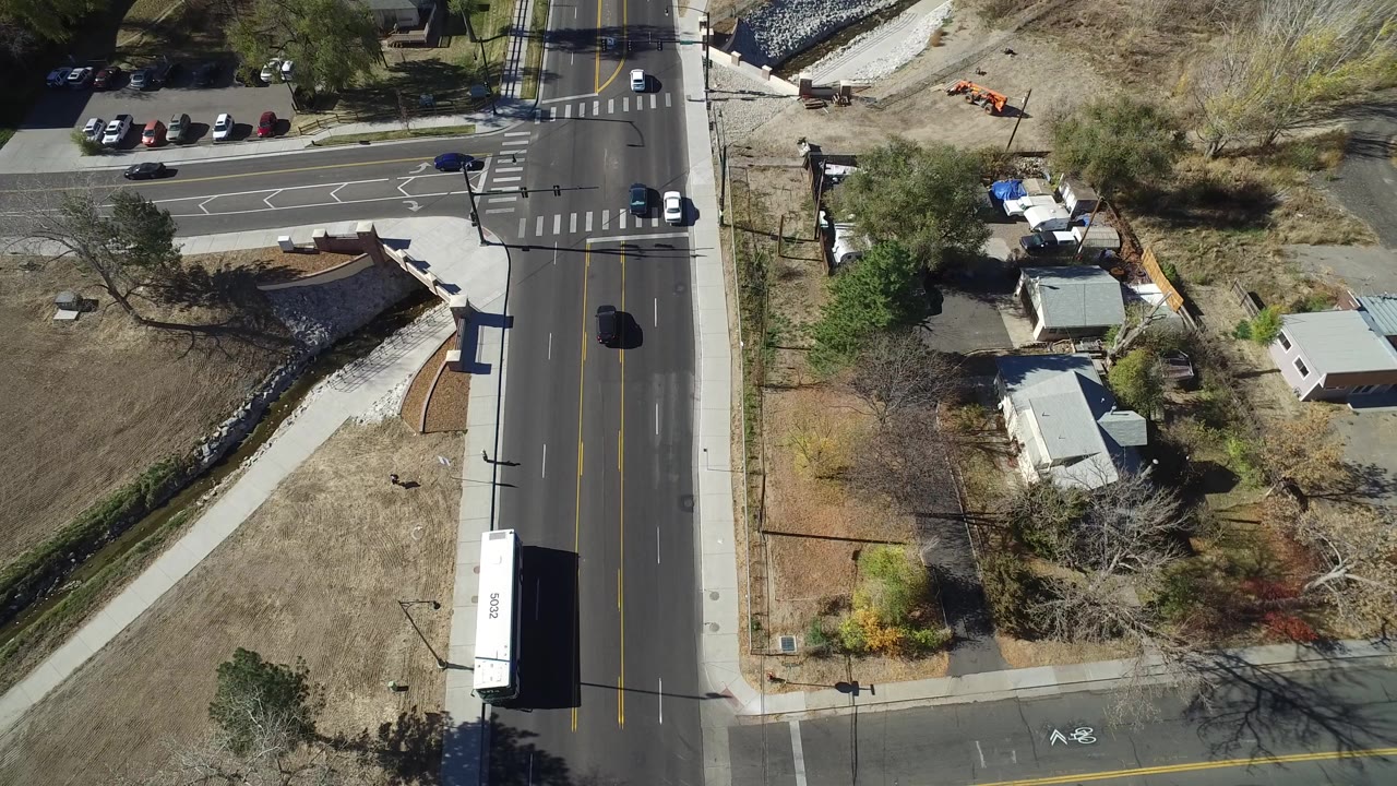 Overhead view of a road intersection with cars, dry land, buildings, and trees.