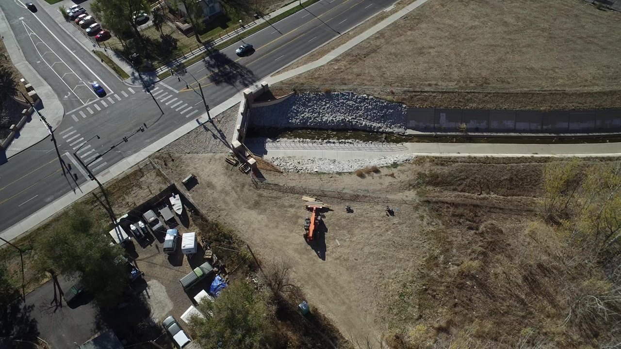 Overhead view of an intersection, drainage channel, dry grass, trees, and orange construction equipment.