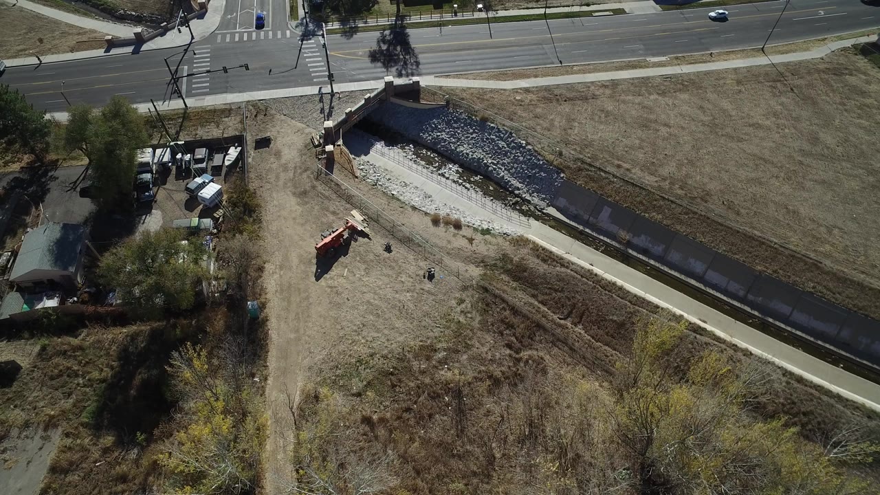 Aerial view of a road, drainage channel, dry grass, and an orange excavator.