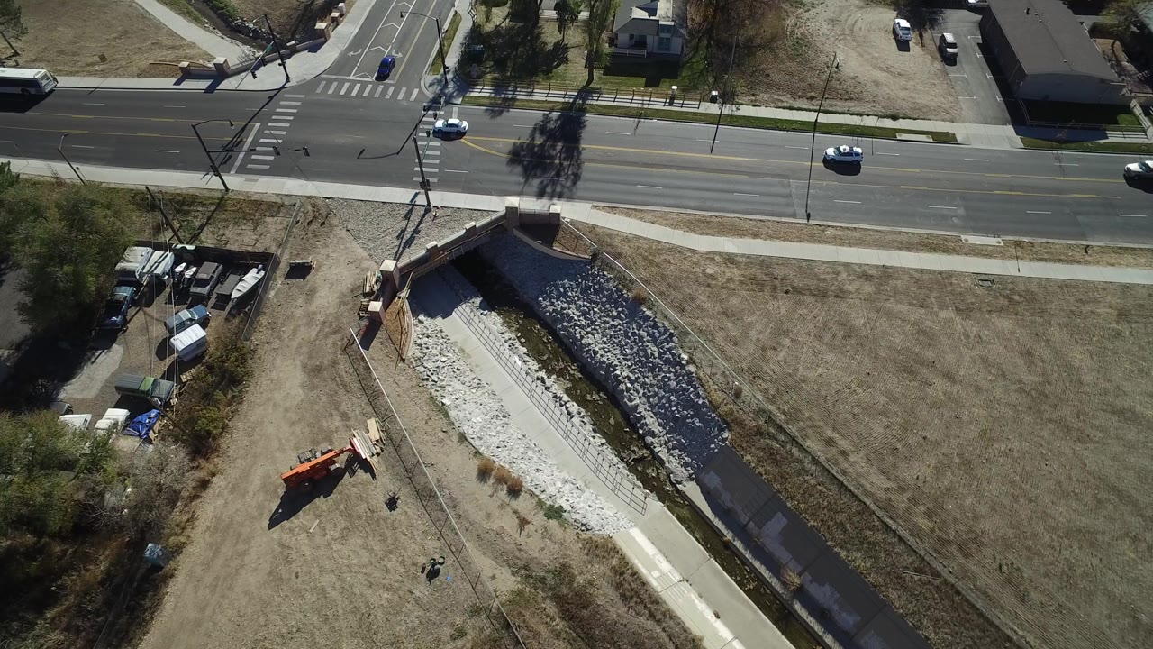 Aerial view of a suburban road, sidewalks, drainage channel, and light traffic.