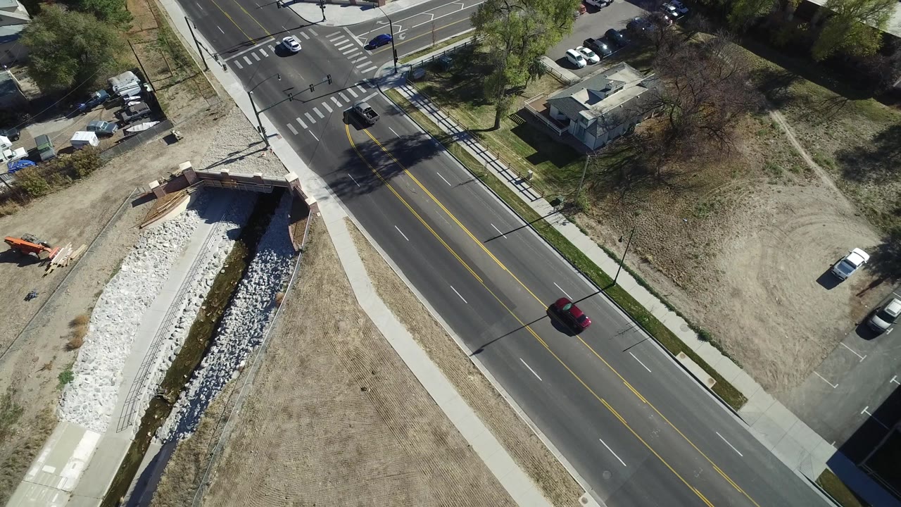 Aerial view in Westminster, Colorado with the road centered between sidewalks, a red car on the pavement, parked vehicles nearby, open grass lots, and no visible people.