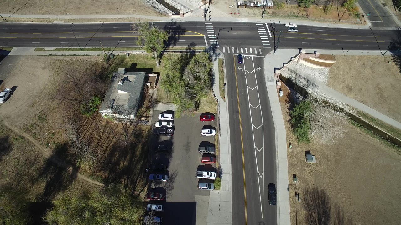 Top-down road intersection with a few cars and surrounding lawns.
