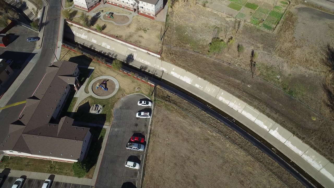 Overhead view of road, bridge, parking lot, white buildings, and dry grass.