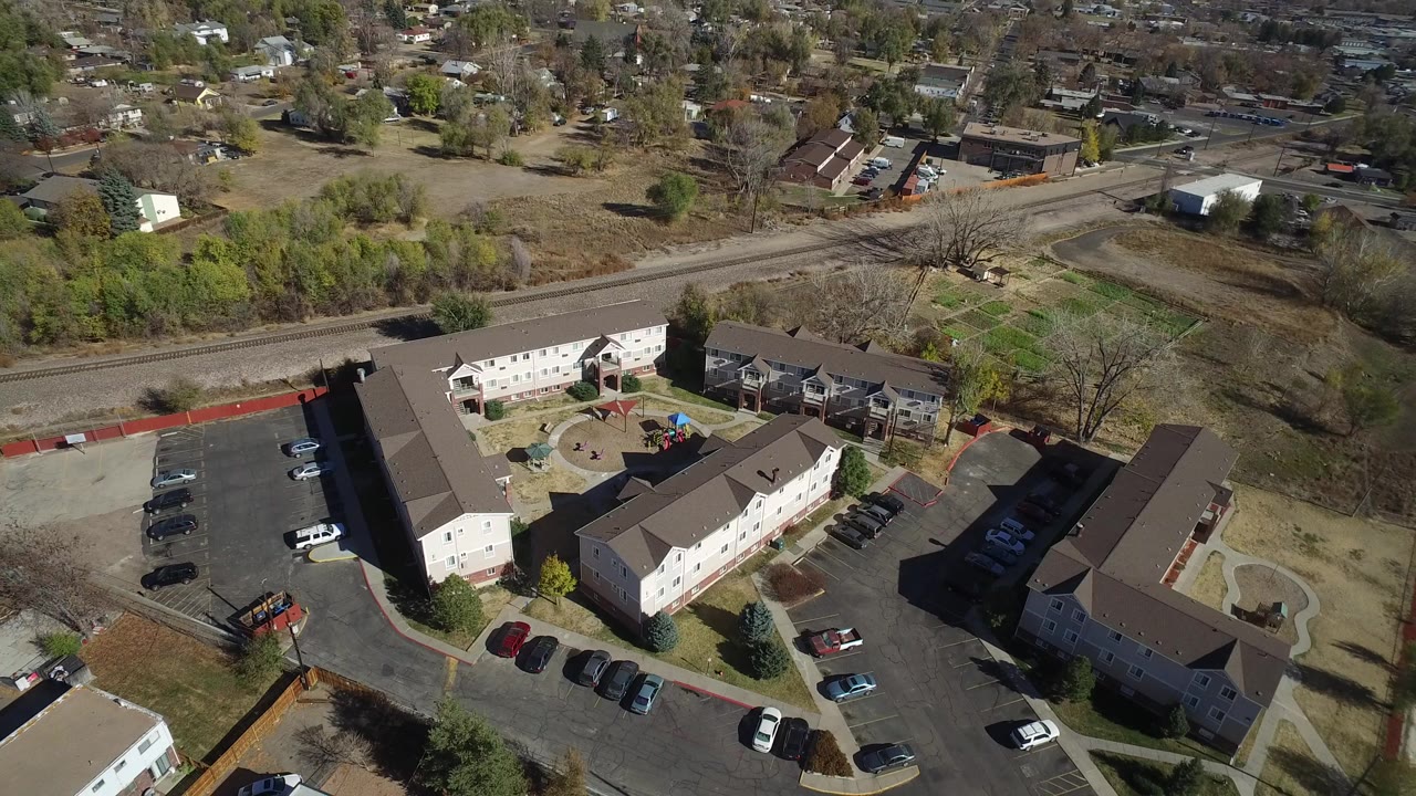 Aerial view of an apartment complex with parking lots, roads, trees, and rail tracks nearby.