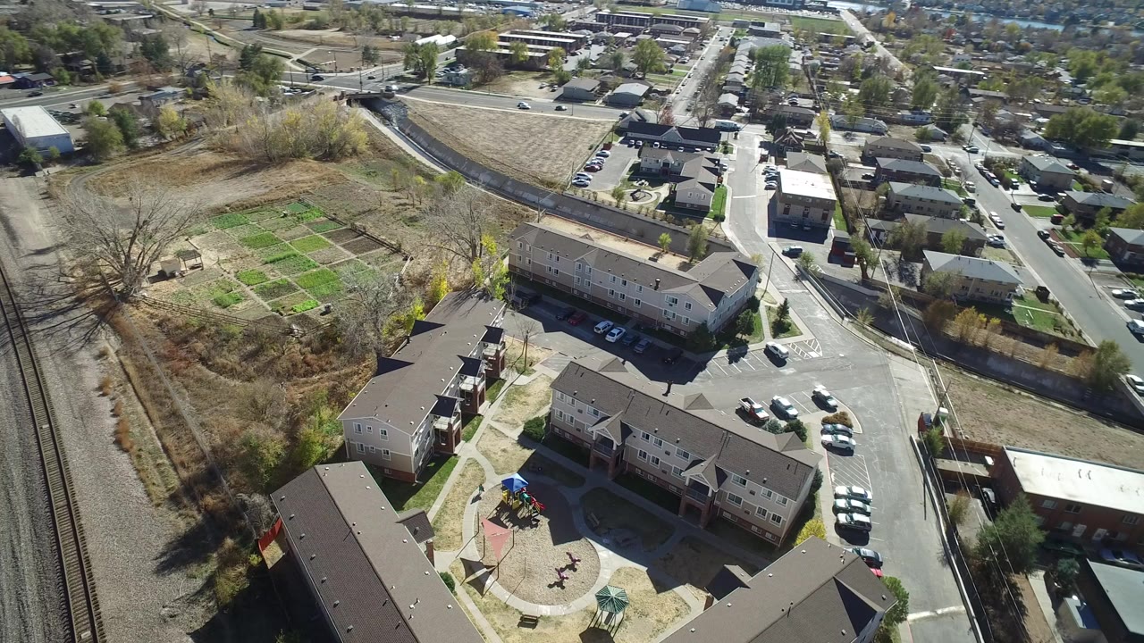 Aerial view over apartment buildings, roads, rail tracks, and garden plots.