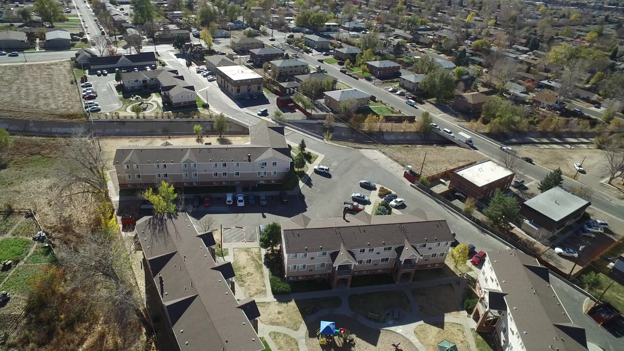 High aerial view over Westminster, Colorado with apartment buildings in the foreground, a road intersection, parked cars, open lots, and no visible people.