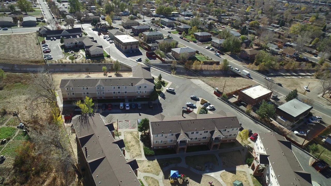 Aerial frame over Westminster, Colorado showing the same residential complex from a slightly shifted angle, with a road running past open land and no visible people.