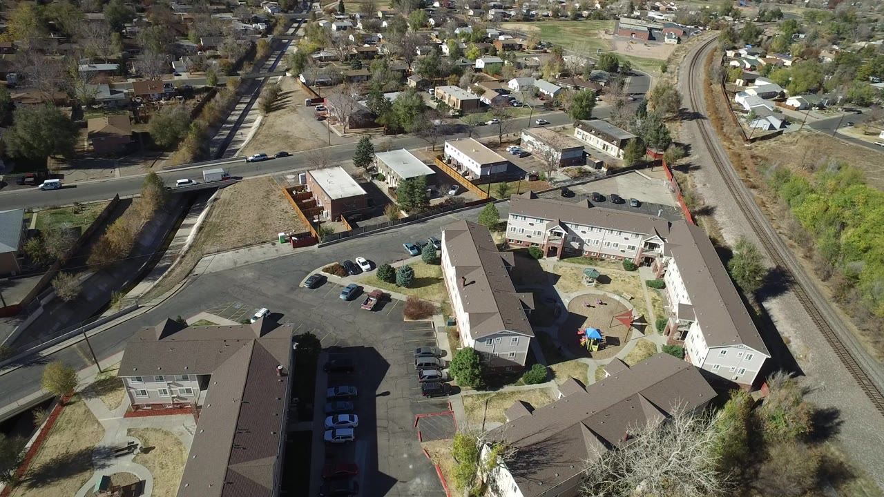 Aerial view of apartment buildings, parking lots, road bridge, and rail tracks.