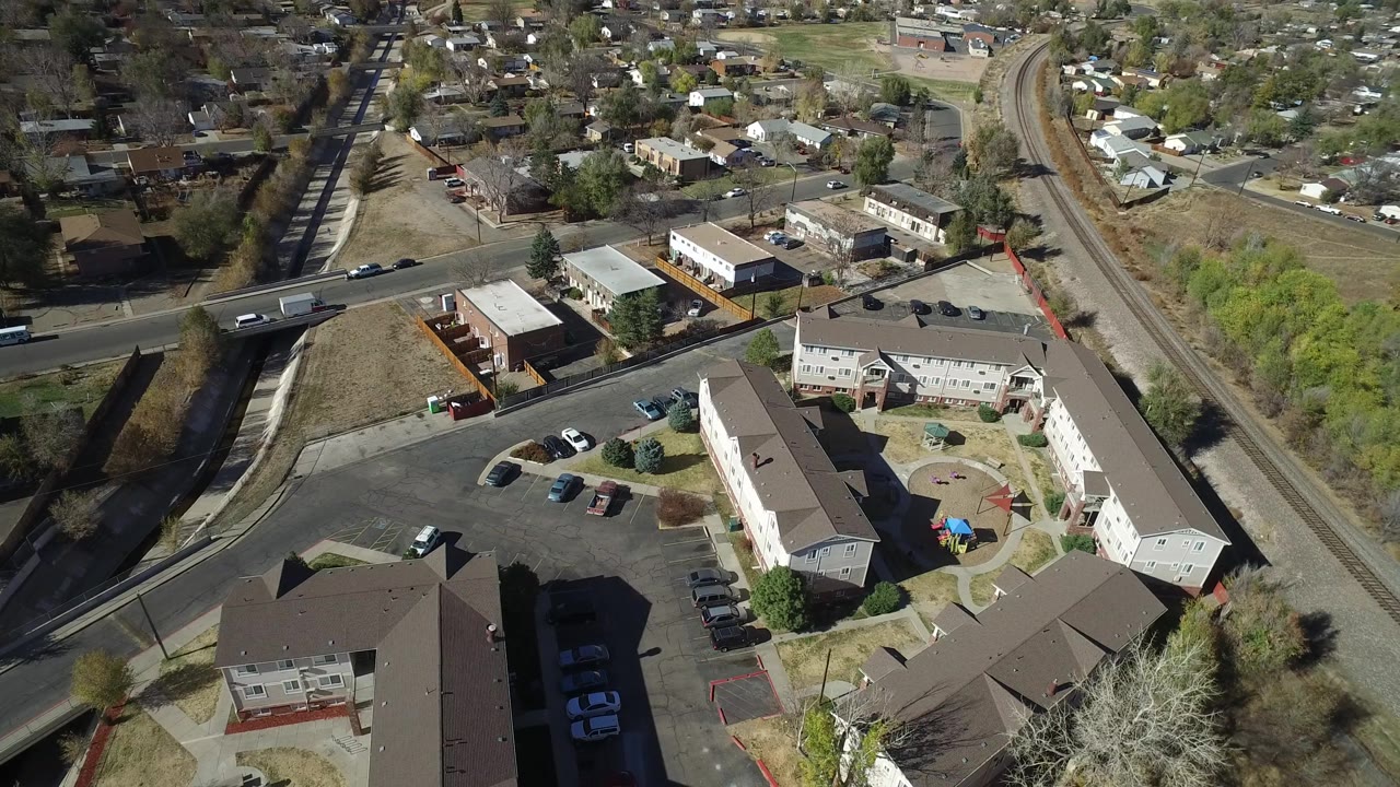 Aerial view of apartments, curved driveways, rail tracks, and nearby homes.