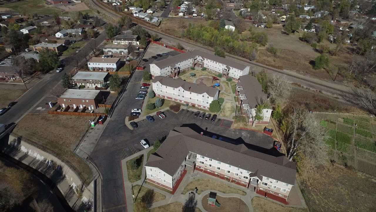 Aerial view of townhome buildings, roads, parked cars, and dry grass lots.