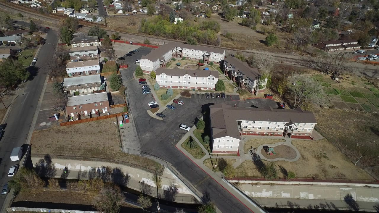 Aerial frame over Westminster, Colorado showing low-rise apartment buildings, paved parking areas, nearby roads, a canal edge, and no visible people.