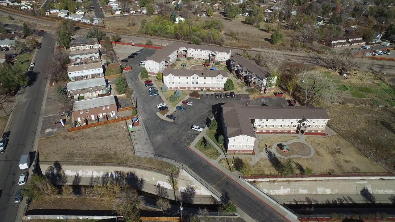 Aerial neighborhood view with apartment buildings, roads, trees, and distant homes.