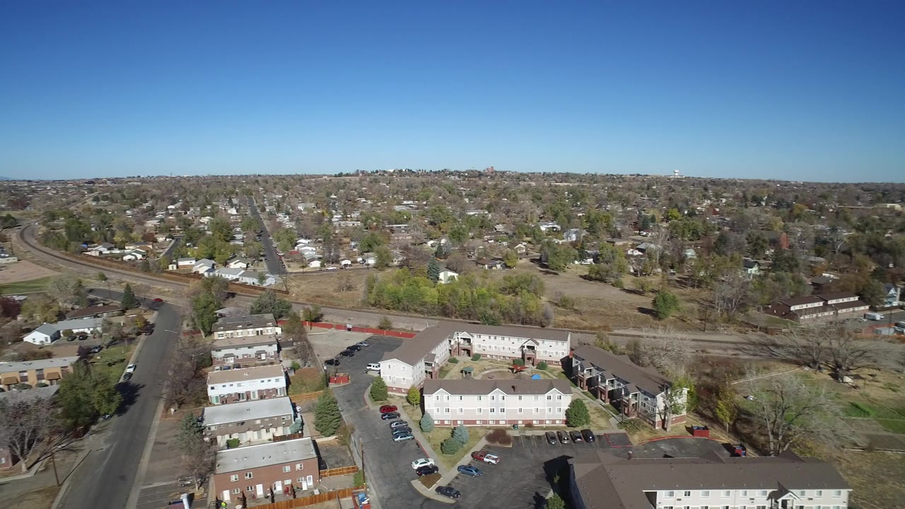 Aerial view over suburban houses, streets, and open lots under a blue sky.