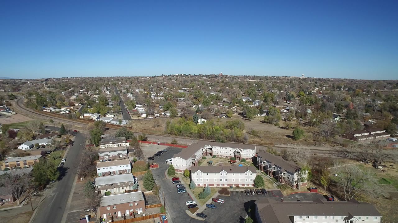 The aerial view continues across Westminster, Colorado with clustered homes, apartment-style buildings, parking areas, leafless trees, open land, and no visible people.