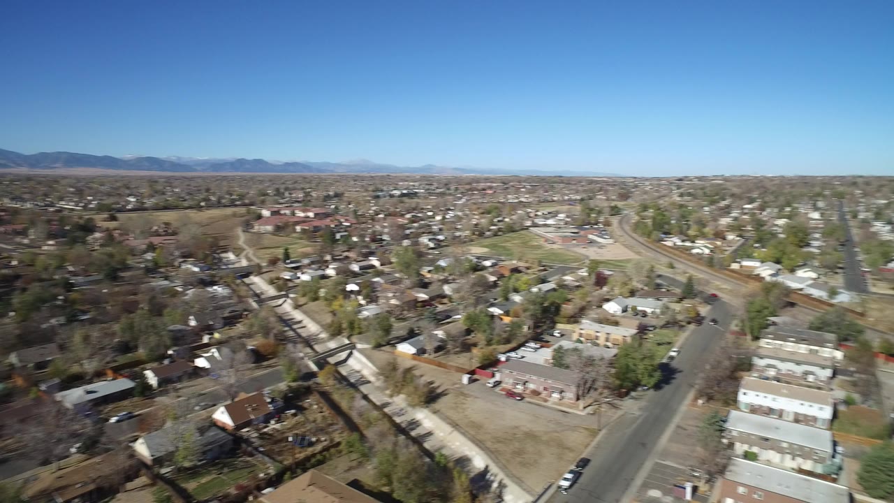 Aerial view of suburban homes, roads, trees, and distant hills under a clear blue sky.