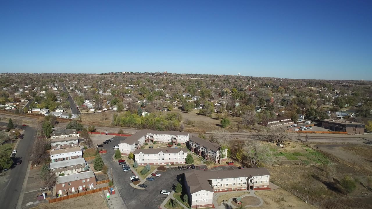 Aerial view of apartment buildings, streets, and suburban houses under blue sky.