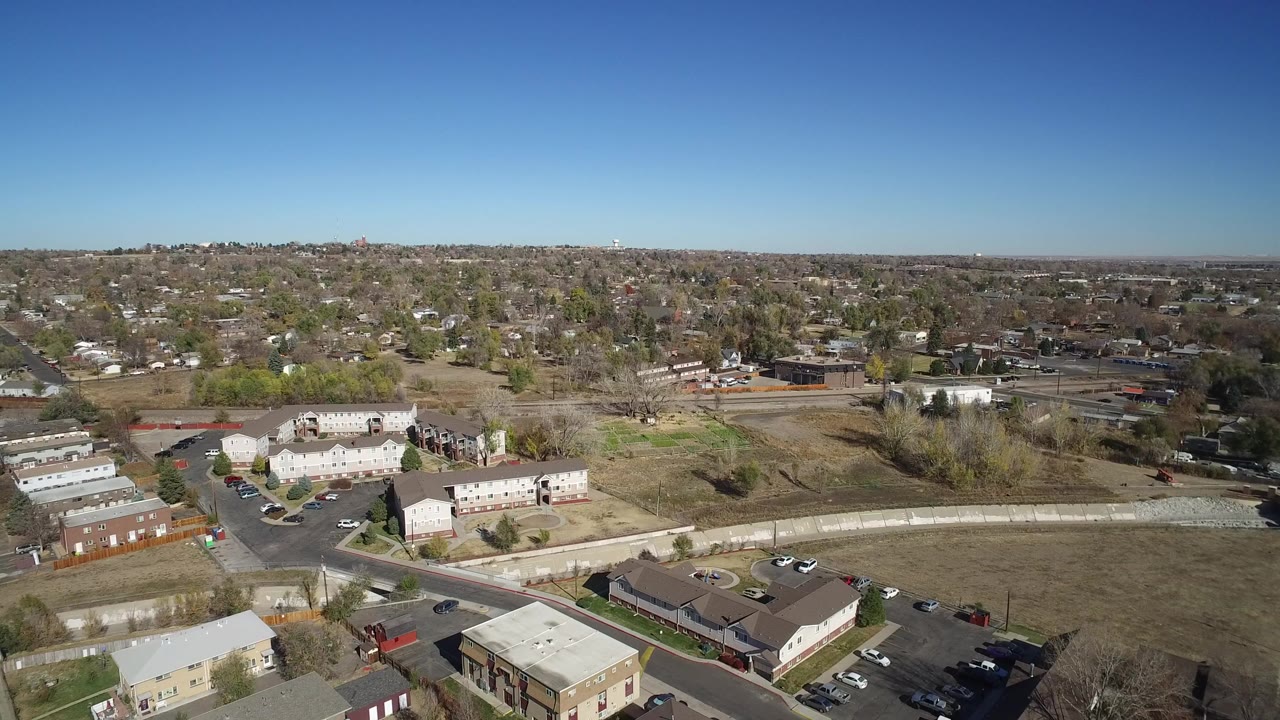 Aerial view of suburban homes, apartments, open grass, and trees under blue sky.
