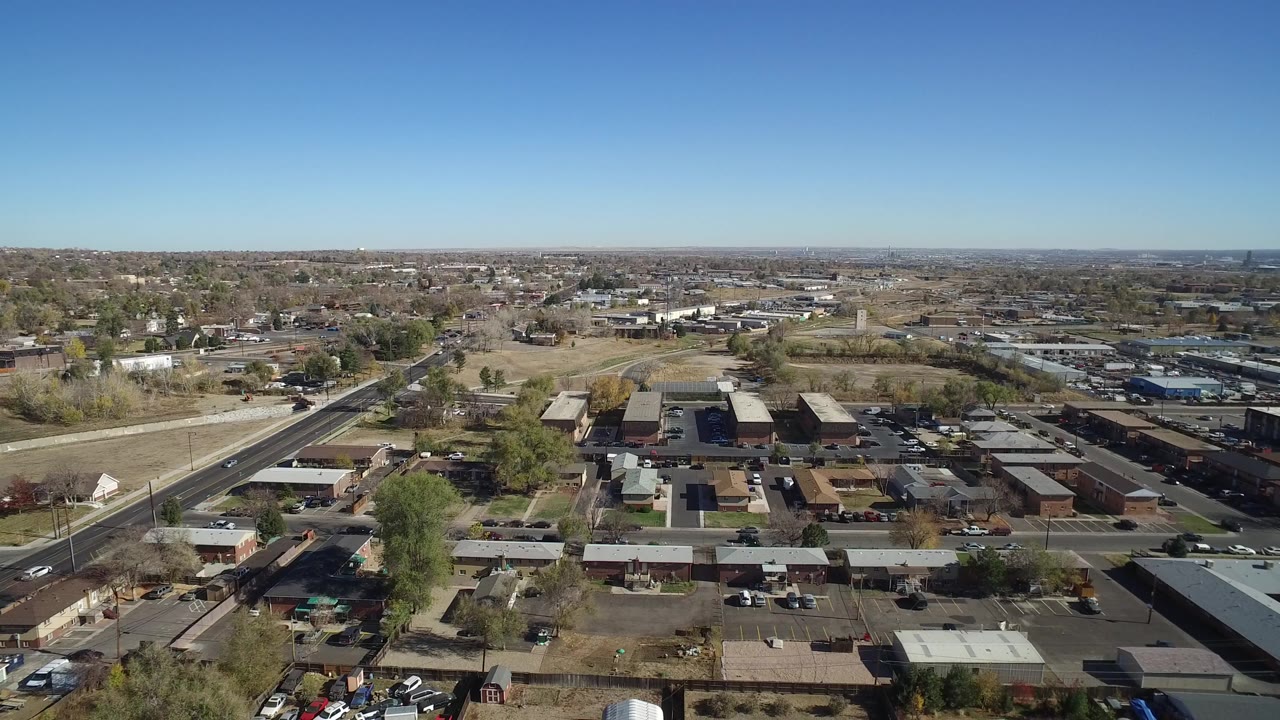 High aerial view over suburban streets, homes, and low buildings under a blue sky.