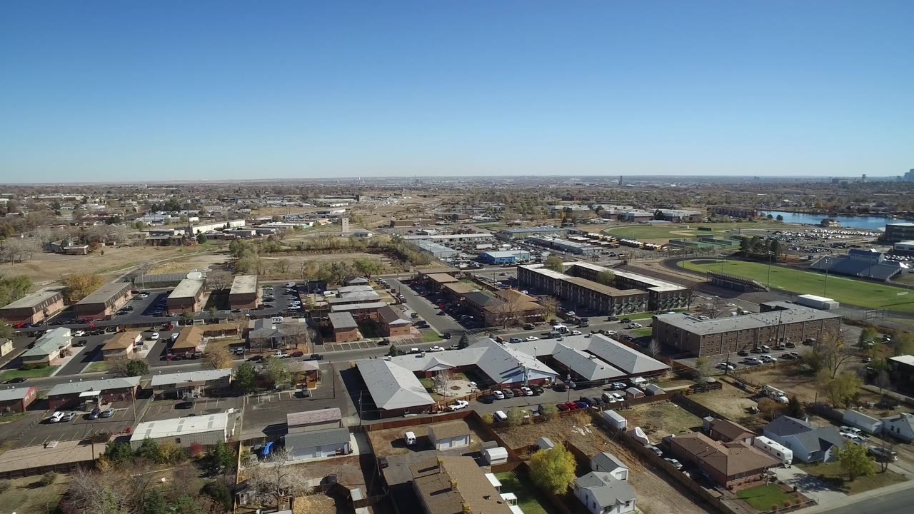Second frame shows Westminster, Colorado from above with more of the road grid and low commercial buildings visible, a sports field near the center-right, water in the distance, and no visible people.