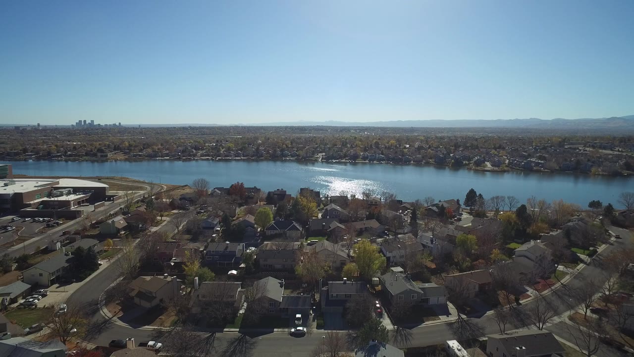 Wide aerial view of homes, a lake, distant skyline, and blue sky.