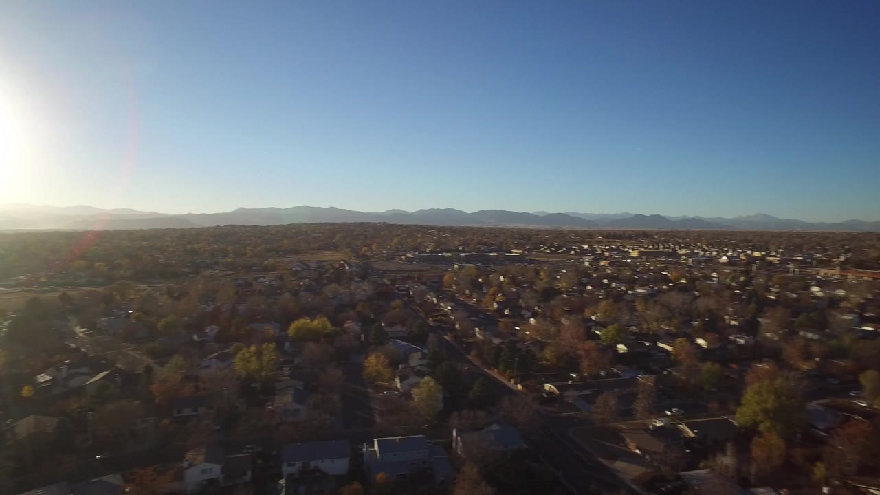 Aerial view over suburban houses with sun glare and distant mountains.