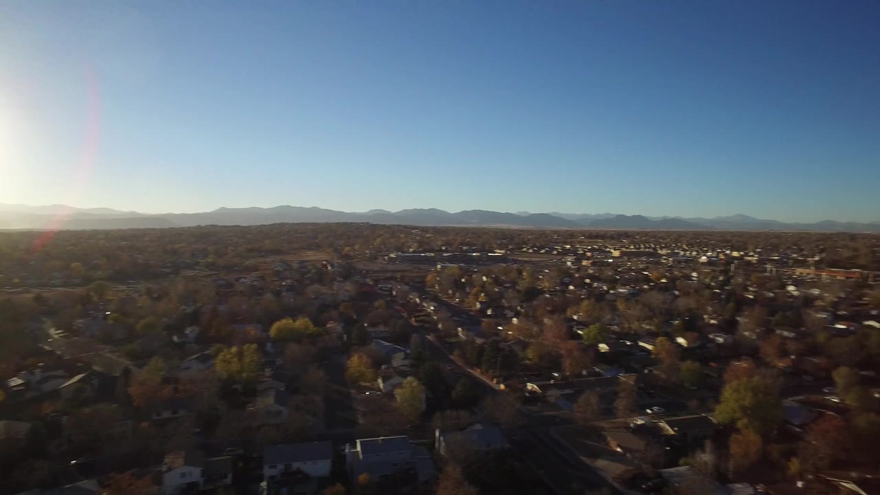 Aerial view across Westminster, Colorado residential blocks with rooftops and trees in the foreground, a low mountain range in the distance, and no visible people.