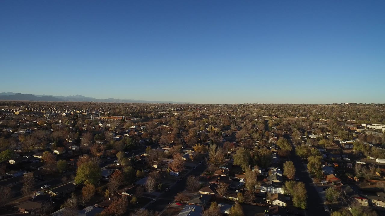 Wide aerial view over wooded suburban homes under a blue sky.