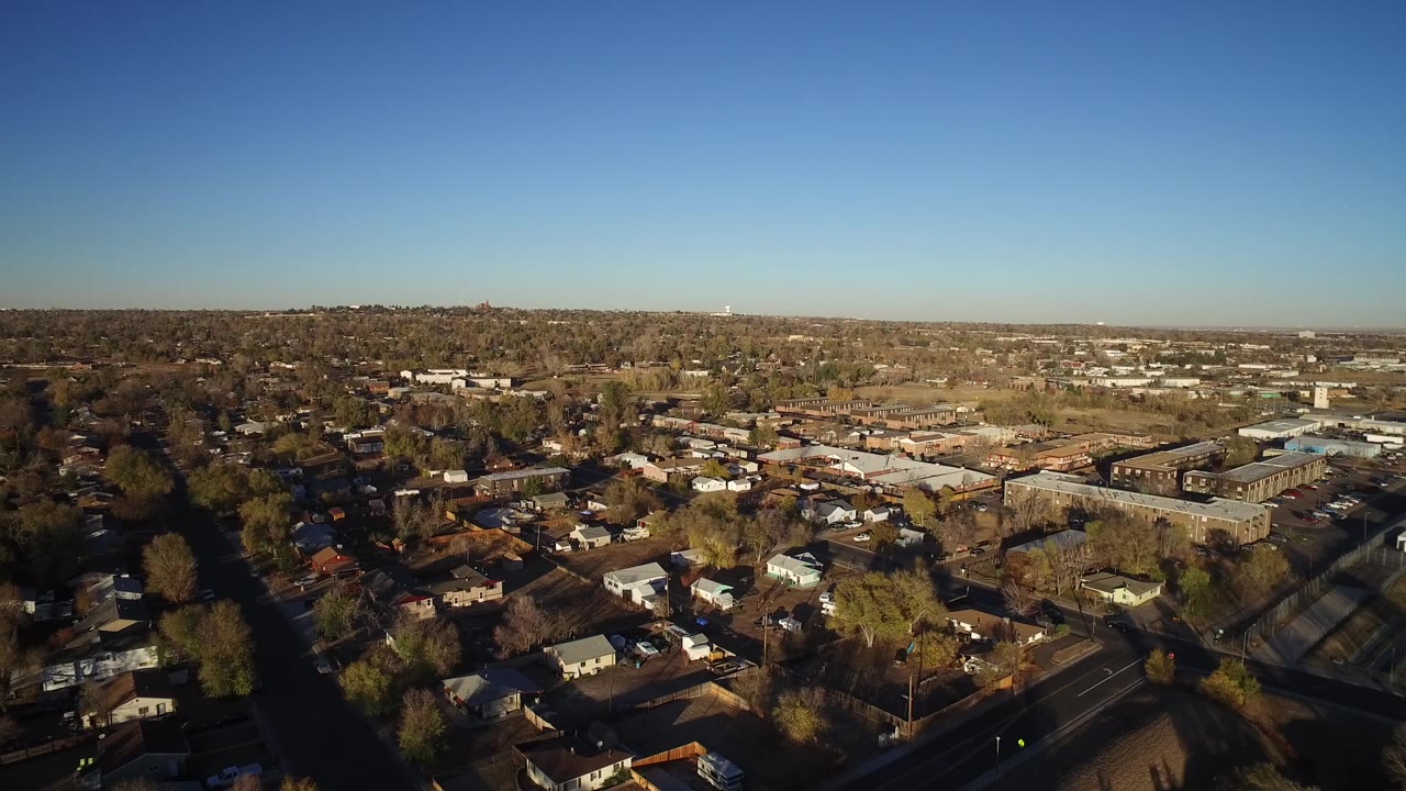 Aerial view in Westminster, Colorado with rooftops and shaded streets in the foreground, larger buildings in the midground, and no visible people.