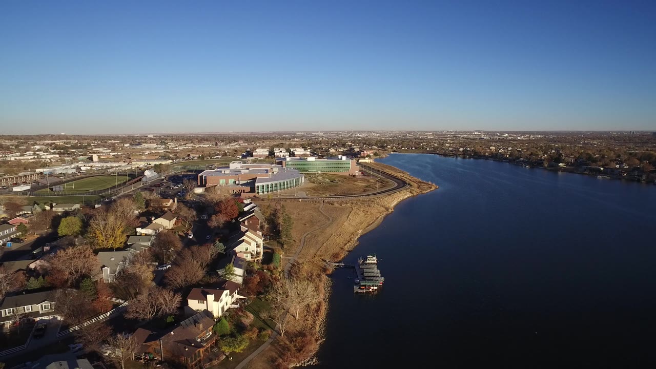 Aerial view of a blue lake beside suburban homes and a large building complex.