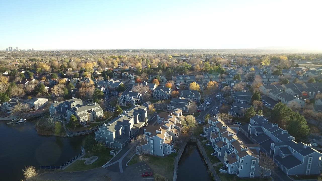 Aerial view in Westminster, Colorado with the lake on the left, clustered homes below, autumn-colored trees across the neighborhood, and no visible people.