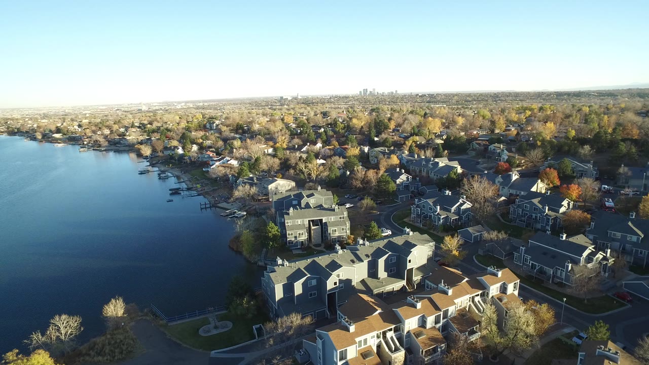 Aerial view of lakeside homes, trees, and blue water under clear sky.