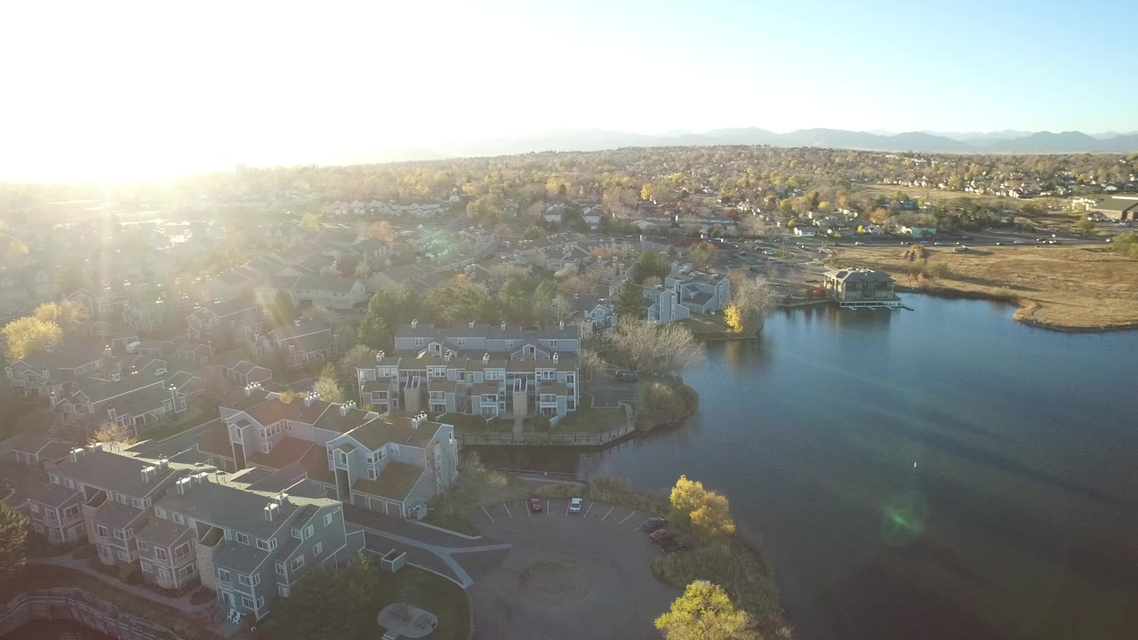 Aerial view of homes beside a pond with sun glare and distant mountains.