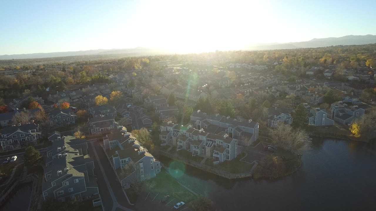 Aerial view of apartment buildings, ponds, trees, and bright low sun.